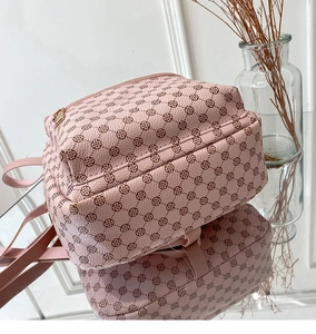 Pink faux leather backpack with brown clover pattern on a reflective surface