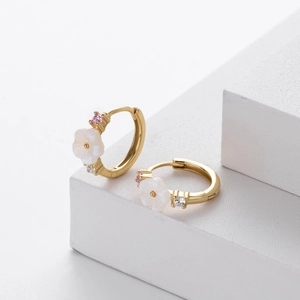 Macro shot of gold floral hoop earrings with white petals and pink zircon on stone stand