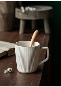 Close-up of a white ceramic mug with vertical stripes and a wooden spoon inside