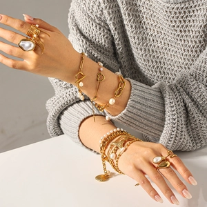 Detail of layered gold stainless steel bracelets and freshwater pearl rings for women