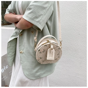Detail of round straw crossbody bag featuring pink floral embroidery and leather strap