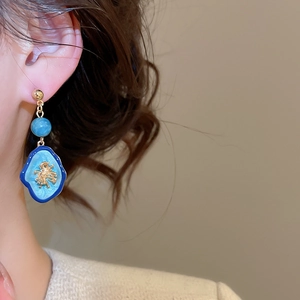 Détail macro de boucles d'oreilles vintage en émail bleu avec relief corail doré sur mannequin