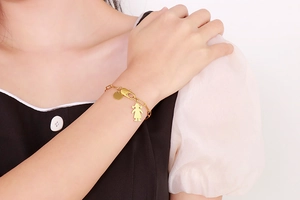 Détail d'un bracelet en acier titane doré avec breloque silhouette de fille et disque rond