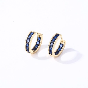 Detail view of gold huggie earrings featuring baguette-cut blue gemstones and bead edges
