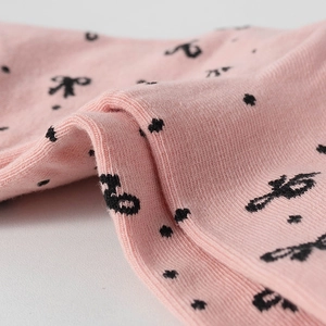 Macro detail of pink knit cotton fabric featuring black polka dots and a bow pattern