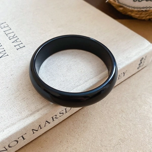 Polished black resin bangle resting on a vintage book showing glossy reflective finish