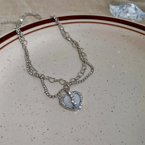 Detail of a double-layered heart necklace with a light blue opal stone on a ceramic plate
