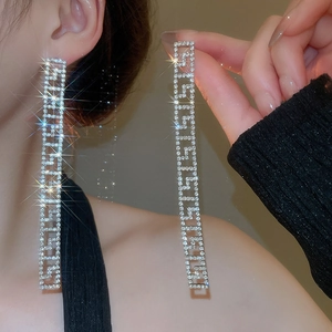 Dettaglio di lunghi orecchini quadrati in argento con cristalli e design a chiave greca