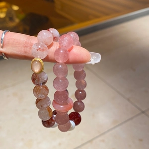 Close-up of strawberry quartz and beaded bracelets held by hand with warm lighting