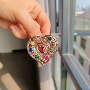 Detail of hand holding a golden heart brooch with colorful rectangle crystal stones