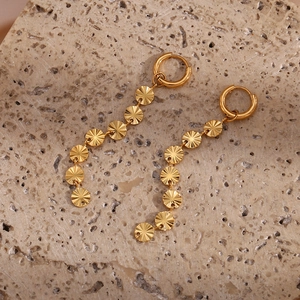 Detailed macro shot of 18K gold-plated snowflake sequin tassel earrings on stone