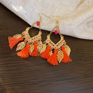Detail showing bohemian leaf charms and vibrant orange cotton tassels on gold drop earrings