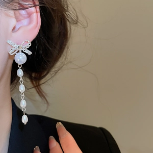 Close-up of elegant bow earrings with pearls and rhinestones on a female model