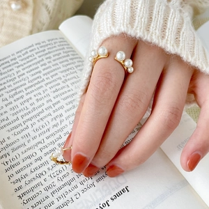 Detail of gold pearl open ring worn on hand with cozy knit sweater and book background