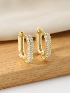 Macro shot of gold U-shaped earrings with micro-pave cubic zirconia on a warm background