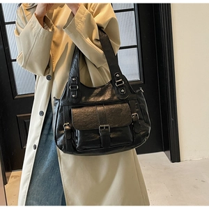 Detail of black leather hobo bag with multiple buckle pockets shown with a beige trench coat