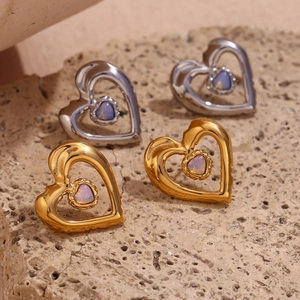 Macro detail of heart-shaped gold and silver earrings with opal stone on stone texture