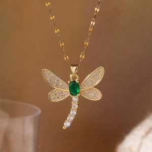 Gold dragonfly necklace with green gemstone and sparkling zircons on a soft brown background