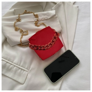 Detail of red square hardshell handbag with gold metal chain strap on a white blazer