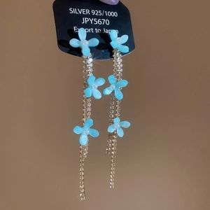 Detailed view of silver flower earrings with light blue petals and hanging rhinestone tassels