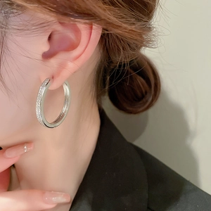 Close-up of a silver geometric hoop earring with zircon inlay worn by a model