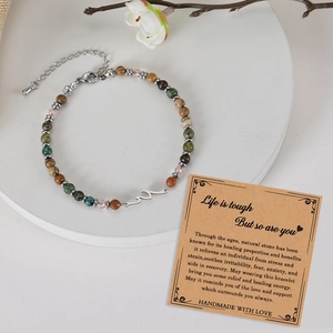 Natural stone beaded wave bracelet with cross charm and gift card on a white stand