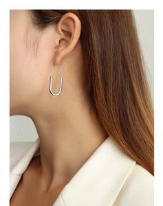Close-up of a minimalist silver safety pin earring worn by a model on a beige background