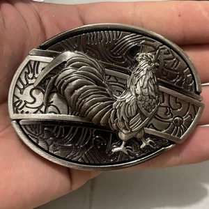Detailed relief of a rooster on a vintage silver oval belt buckle held in hand