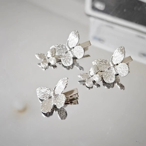 Close-up of three silver butterfly hair clips with textured finish on mirror surface