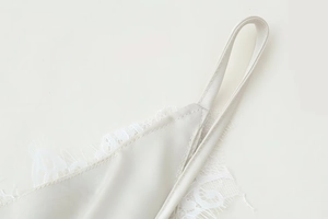 Macro view of creamy white satin fabric with delicate eyelash lace trim and stitching