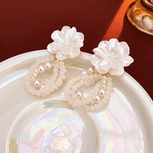Close-up of gold floral earrings with woven pearls on an iridescent ceramic tray
