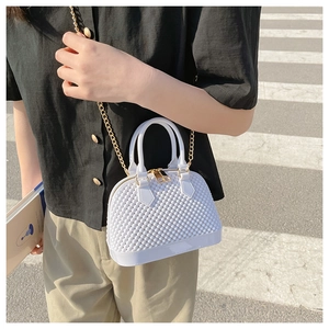Detail of white PVC shell bag with diamond texture and gold chain on model