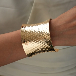 Detailed view of wide gold woven cuff bracelet with hammered metal texture on model's wrist