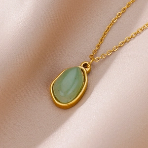 Macro shot of 18K gold plated necklace with a pear-shaped green gemstone on silk fabric