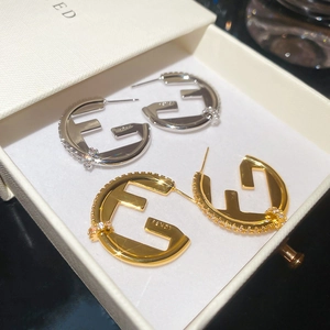 Macro shot of gold and silver C-shaped hoop earrings with F logo and cubic zirconia