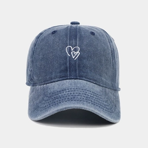 Détail macro de la broderie cœur blanc sur la casquette en denim bleu délavé