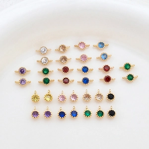 Gold plated colorful cubic zirconia charms and connectors on a white ceramic tray