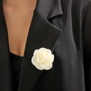 Detailed view of a white camellia fabric flower brooch styled on a black blazer lapel
