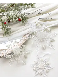 Three-piece acrylic glitter snowflake ornaments on white satin with pine cones