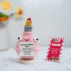 Macro shot of handmade crochet emotional support bomb doll with a Christmas card on wood base