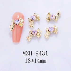 Macro detail of 13x14mm golden bow nail charms with pink heart-shaped crystal rhinestones