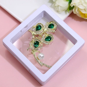 Detailed macro view of a gold brooch with green gems and a pearl in a display box