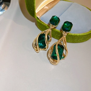 Detail of emerald green teardrop earring with gold spiral design on green velvet box