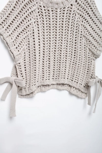Gros plan sur la maille épaisse et le détail du nœud latéral sur le pull ajouré beige