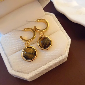 Close-up of golden metal earrings with round brown tiger eye stone on white velvet box