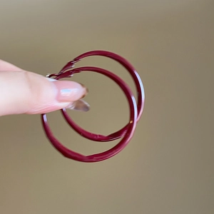 Close-up of oversized deep red circular hoop earrings with a glossy lacquered finish