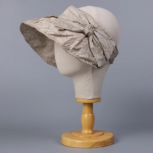 Close-up of sun hat with large bow detail and textured fabric on wooden head stand