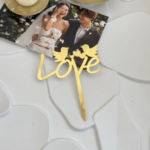 Close-up of golden LOVE acrylic cake topper with birds on a romantic wedding display
