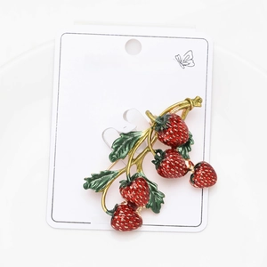 Detailed view of enamel strawberry brooch with red fruit and green leaves on card