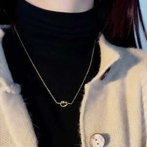 Minimalist 18K gold plated knot pendant necklace worn over a black turtleneck sweater